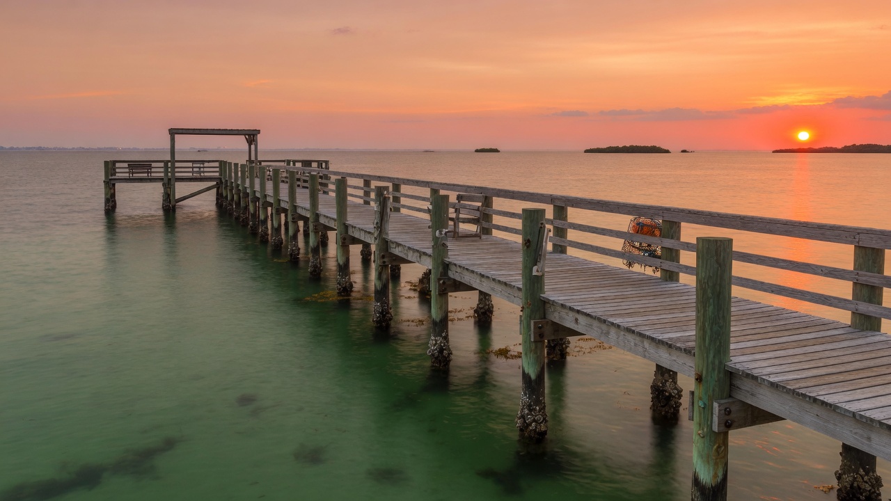 A long wooden pier reaching out over open Gulf water under a clear sky on the Florida coast
